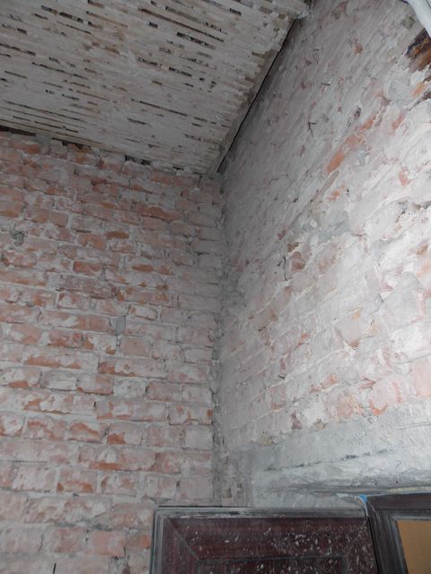 Colț de încăpere cu pereți de cărămidă aparentă și plafon cu grinzi și scândură de lemn.