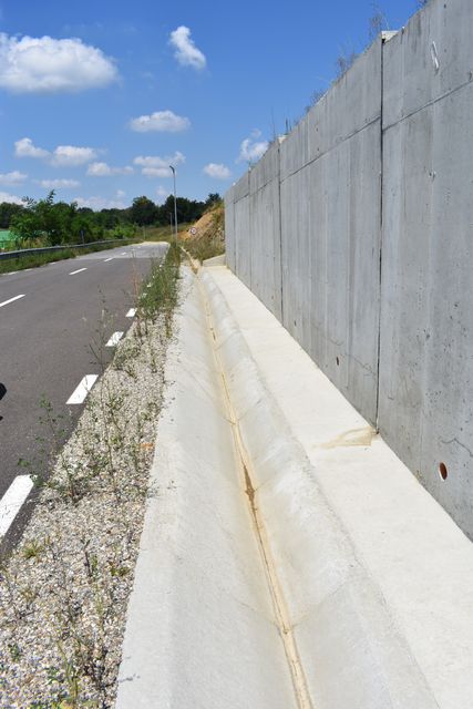 Zid de beton de-a lungul unui drum asfaltat, cu rigolă betonată la baza lui